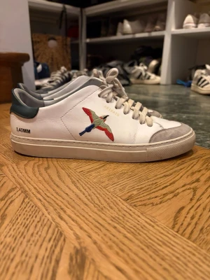   Axel Arigato skor - Snygga vita sneakers från Axel Arigato med broderad fågel i rött, skorna har lite små skavanker se bilder, men annars väldigt fina. Kom med prisförslag!