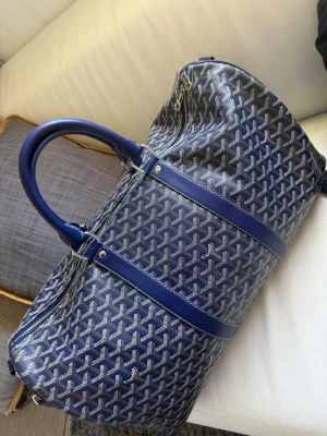 Blå Goyard weekendbag - Snygg blå weekendbag från Goyard med klassiskt mönster och detaljer i läder. Väskan har två rejäla handtag och dragkedja upptill. Perfekt för resor när du vill ha både stil och funktion.