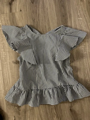 Rutig blus med volangärmar - Snygg blus i blåvitt rutigt mönster med volangärmar och volang nertill. Blusen har en luftig passform och är perfekt för dig som gillar en söt och trendig stil.