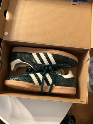 Adidas Samba OG gröna sneakers - Adidas Samba OG sneakers i mörkgrönt med vit sula och klassiska vita stripes på sidorna. Ovandelen har en texturerad, nästan ormskinnsliknande yta. Skorna kommer med både gröna och vita skosnören. Perfekta för dig som vill sticka ut med en ikonisk modell.OBS! Helt nya, fått i present o är tyvärr lite för stora för mig. Helt oanvända vara testade en gång. Köpta från herr båda könen kan använda de.