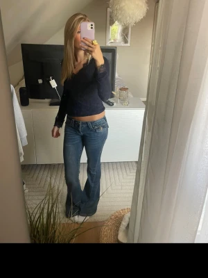 Blå bootcut jeans från True Religion - Säljer ett par blå bootcut jeans från True Religion med låg midja och klassiska detaljer på bakfickorna. Syns lite på användning längst ner på jeansen 