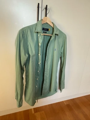 Ralph Lauren skjorta - Klassisk grön skjorta från Polo Ralph Lauren med lång ärm och knappar framtill. Skjortan har en broderad logga på bröstet och är tillverkad i mjuk bomull. Tags och qr kod finns. Storlek S/M