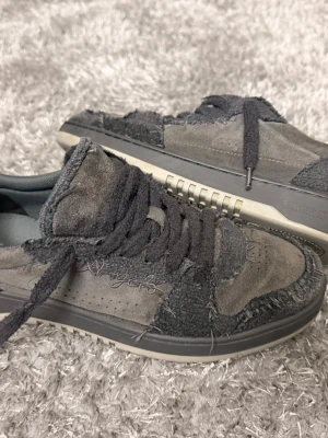 Grå Axel Arigato sneakers - Unika sneakers från Axel Arigato i olika nyanser av grått med slitna detaljer och råa kanter. Skorna är låga och har en cool mix av mocka och textilmaterial. Tjocka grå skosnören och broderad logga på sidan. Original box ingår med inga defekter på skorna i någon nivå.