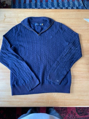 tröja Polo Ralph Lauren - Snygg mörkblå kabelstickad tröja från Polo Ralph Lauren med halv dragkedja och hög krage. Tröjan har långa ärmar, ribbade muddar och är gjord i ett mjukt material som passar perfekt till jumna dagar.
