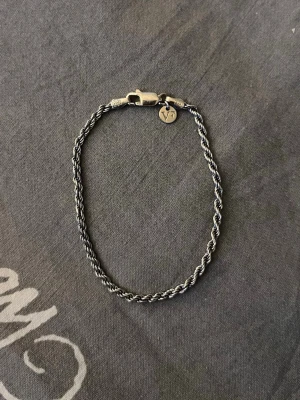 Silverfärgat tvinnat armband från guldfynd x viktorfrisk - Snyggt armband från guldfynd x viktorfrisk silverfärgad metall med tvinnad kedja och en liten rund bricka med Vf-logga vid låset. Perfekt accessoar för att lyfta din stil med en enkel men stilren detalj. Låset är av karbinhake-modell. Låda till armbandet saknas 