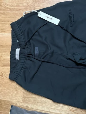 Svarta Essentials mjukisbyxor - Svarta mjukisbyxor från Essentials med elastisk midja och dragsko. Byxorna har en avslappnad passform och är tillverkade i mjukt material. Diskret Essentials-logga tryckt på benet. Perfekta för en chill och stilren look.