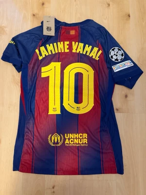 Lamine Yamal #10 – Player Edition (storlek M) - Lamine Yamal #10-tryck. Player Edition med Champions League patch på ärmen. Storlek M. Helt ny och aldrig använd. Säljs i befintligt skick. Skickas snabbt! 🚚💨  Mått för denna tröja (storlek M): (Uppmätta av leverantör – viss variation kan förekomma) • Halva bröstmåttet: 51 cm • Tröjans längd: 72,5 cm • Ärmbredd: 22,5 cm • Axelbredd: 43 cm • Ärmlängd: 39 cm • Manschettbredd: 18 cm  🔥 Player Edition-modell – tajtare passform än vanliga supportertröjor.