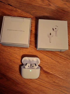 Apple AirPods 4 med laddningsetui - Säljer ett par vita Apple AirPods 4 med trådlöst laddningsetui. Hörlurarna har en stilren och kompakt design i blank plast och levereras i originalförpackning. Perfekta för musik, samtal och smidig anslutning till iPhone eller andra Apple-enheter.