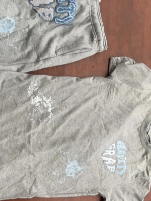 Grått bodyset med blått tryck - Säljer ett grått bodyset med kortärmad topp och matchande underdel. Setet har blått texttryck och stänkdetaljer framtill för en cool, avslappnad look. Materialet är mjukt och stretchigt, perfekt för en bekväm känsla hela dagen.