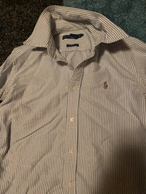 Randig skjorta från Ralph Lauren - Snygg blåvit randig skjorta från Ralph Lauren med klassisk krage och broderad logga på bröstet. Skjortan är i super slim fit och tillverkad i bomull. Perfekt för dig som gillar stilrena och tidlösa plagg.