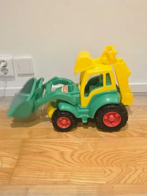 Grön och gul leksaksgrävare Polesie - Säljer en färgglad leksaksgrävare från Polesie i plast. Grävaren är grön och gul med röda hjul och har både skopa fram och bak. Perfekt för lek på golvet eller i sandlådan. Enkel att köra runt och använda för olika bygglekar.