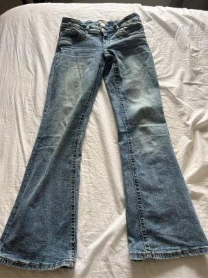 Blå bootcut jeans från H&M - Säljer ett par ljusblå bootcut jeans från H&M med klassisk femficksmodell och slitna detaljer. Jeansen har normal midja och är tillverkade i denim med lätt stretch. Perfekta för dig som gillar retrovibbar och en avslappnad look.