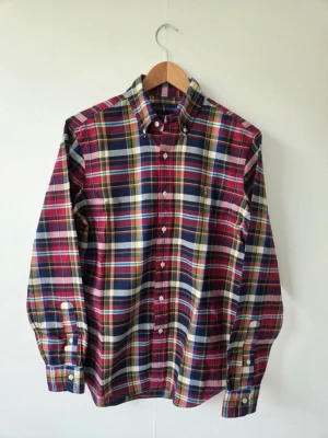 Rutig skjorta från Ralph Lauren stl s - Klassisk långärmad skjorta från Ralph Lauren i rött, blått, grönt och vitt rutigt mönster. Skjortan har button-down krage, vita knappar och den ikoniska broderade loggan på bröstet. Tillverkad i mjuk bomull för en bekväm känsla.