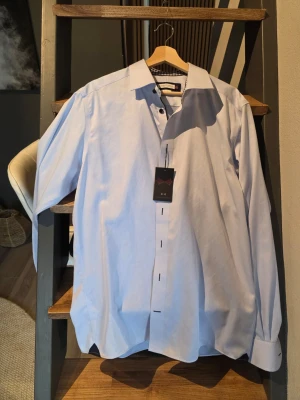 Ljusblå klassisk slim fit skjorta från j. Harvest & frost - Säljer en stilren ljusblå skjorta från zJ. Harvest & Frost med klassisk krage och knappar framtill. Skjortan har lång ärm och är tillverkad i bomull, perfekt för en clean och snygg look. Passar dig som gillar tidlös stil. 43/44 XL