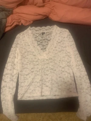 Vit spetsblus från Vero Moda - Säljer en vit långärmad spetsblus från Vero Moda. Blusen har v-ringning med dekorativ spetskant och ett blommigt spetsmönster över hela plagget. den sitter ganska tajt så skulle nog klassa den som en M och L