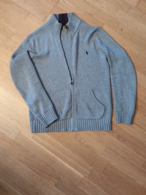 Grå ziptröja från Polo Ralph Lauren - Klassisk grå ziptröja från Polo Ralph Lauren med ribbade mudda. En slags cardigan/zip up. 14-16 i Ralph Lauren barn vilket motsvarar xs. Modellen är 170 cm och väger 60kg