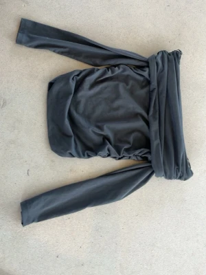 Svart omlottopp från H&M - Säljer en grå topp från H&M. Toppen är axelbandslös och har en tight passform som framhäver figuren. Perfekt för dig som vill ha en trendig och stilren look.