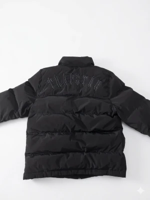 Trapstar jacka - Säljer en svart Trapstar pufferjacka. Den har avtagbar huva, dragkedja fram, broderad logga på ryggen och en patch på bröstet. Varm, stilren och perfekt för kalla dagar.