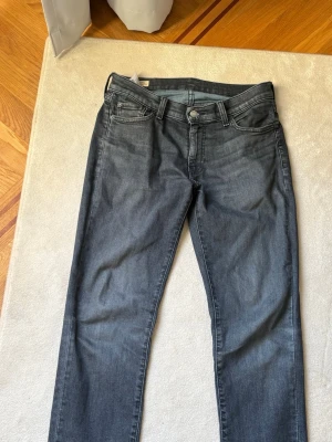 Grå Levi's jeans med rak passform - Snygga grå jeans från Levi's med klassisk femficksmodell och rak passform. Jeansen har en diskret tvättad look, bälteshällor och Levi's ikoniska läderpatch bak i midjan. Perfekta för en avslappnad och stilren outfit.