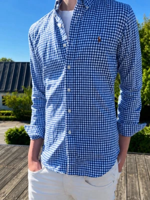 Blårutig skjorta från Ralph Lauren - (Moddelen är 185 och väger 75kg)Klassisk blårutig skjorta från Ralph Lauren med button-down krage och broderad logga på bröstet. Skjortan har lång ärm, knappar framtill och är tillverkad i bomull. Perfekt för en stilren och avslappnad look.