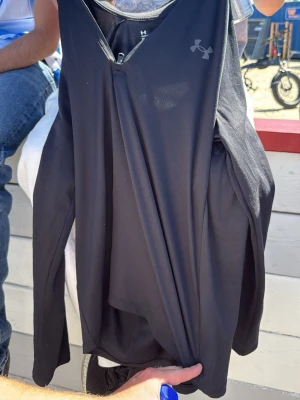 Svart långärmad topp från Under Armour - Snygg svart långärmad topp från Under Armour med diskret logga på bröstet. Tillverkad i ett stretchigt syntetmaterial som passar perfekt för träning. Enkel design med v-ringning och åtsittande passform.