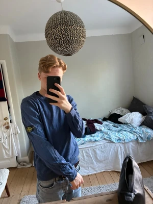 Blå långärmad tröja från Stone Island - Säljer en blå långärmad tröja från Stone Island med den klassiska logotypen på vänster ärm. Tröjan har rund halsringning och är tillverkad i ett mjukt material som passar perfekt till jeans. Enkel och stilren design som funkar till det mesta.