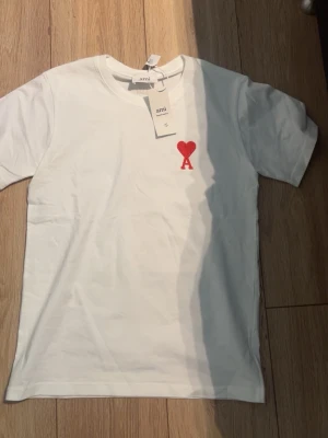 Vit t-shirt med rött hjärta - Vit t-shirt från Ami Alexandre Mattiussi med ett broderat rött hjärta och bokstaven A på bröstet. Klassisk rund halsringning och korta ärmar. Tillverkad i mjuk bomull för en skön känsla.