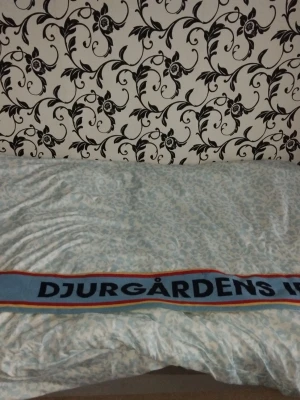 Djurgårdens IF halsduk blå röd gul - Säljer en klassisk supporterhalsduk från Djurgårdens IF med texten 'DJURGÅRDENS' och 'STOCKHOLMSLAGET'. Halsduken har blå botten med röda och gula ränder längs kanterna. Perfekt accessoar för matchdagar eller att visa ditt lagstöd.