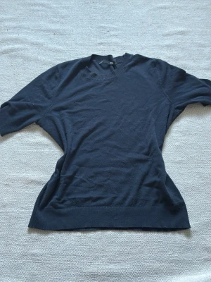 Mörkblå tunn stickad t-shirt  - En mörkblå , tunn stickad tröja från lager 157 med kort ärm och ribbade detaljer vid hals, ärmslut och nederkant. Tröjan har en enkel och stilren design som passar till många olika outfits. Materialet känns mjukt och lätt.