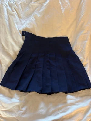 Mörkblå plisserad kortkjol - Snygg mörkblå plisserad kortkjol med klassisk design. Kjolen har bred linning och fina veck som ger ett stilrent intryck. Perfekt för dig som gillar en enkel men trendig look.