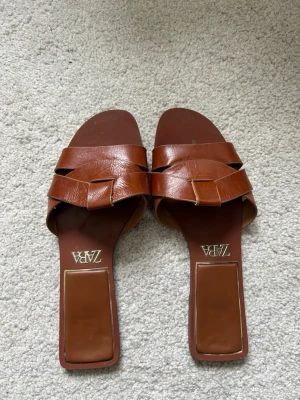 Bruna flätade sandaler från Zara - Säljer ett par bruna sandaler från Zara med flätad design över foten och fyrkantig tå. Bra skick och väldigt bekväma!!