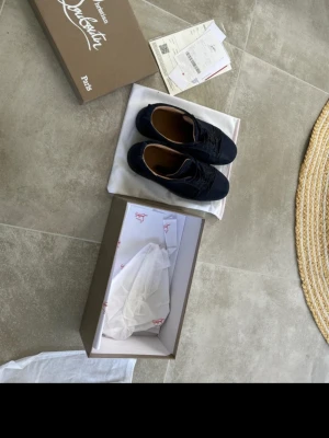 Svarta sneakers från Christian Louboutin - Säljer ett par svarta sneakers från Christian Louboutin med klassisk design och lågt skaft. Skorna har ovandel i mocka och läderdetaljer, samt den ikoniska röda sulan. Kommer med originalkartong och dustbag.