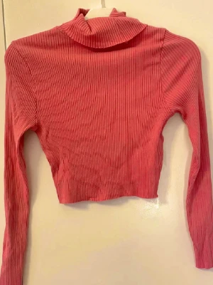 Rosa långärmad ribbad croppad polotopp - Jätte söt långärmad rosa croppad polotopp med ribbad struktur. Perfekt för att styla med höga jeans eller kjol 🩷