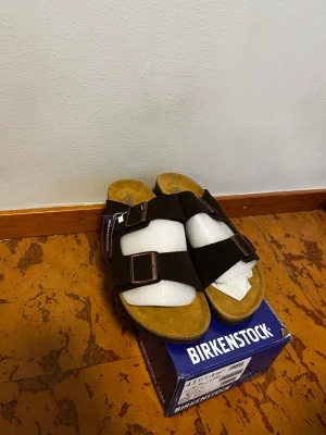 Bruna Birkenstock Arizona sandaler - Säljer ett par klassiska Birkenstock Arizona sandaler i mörkbrunt mocka färg. Storlek 43. Helt nya med kartong!