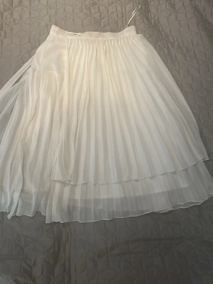Vit plisserad medellång kjol  i chiffong - Säljer en superfin vit medellång kjol  med plisserade lager och flowy känsla. Kjolen  är gjord i ett lätt, skirt material som ger en snygg siluett. Perfekt för dig som gillar en romantisk och stilren look.