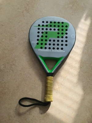 Power Padel padelracket grön/silver - Padelracket från Power Padel i silver och grönt med svart handledsrem och gul grepptejp. Racketen har rund form och många hål i träffytan. Perfekt för dig som gillar padel och vill ha ett snyggt och funktionellt racket.