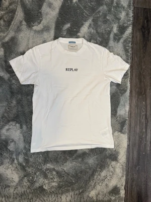 Vit t-shirt från Replay M - Säljer en stilren vit t-shirt från Replay med svart text på bröstet. Klassisk passform och rund halsringning. Storlek M