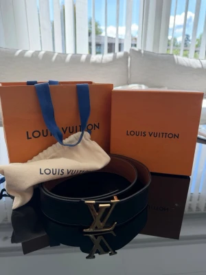 Louis Vuitton svart och brun skärp - Säljer ett exklusivt Louis Vuitton skärp i svart och brunt skinn med den ikoniska LV-loggan i guld framtill. Bältet har en stilren och klassisk design som passar till många olika outfits. Kommer med originalpåse och box.