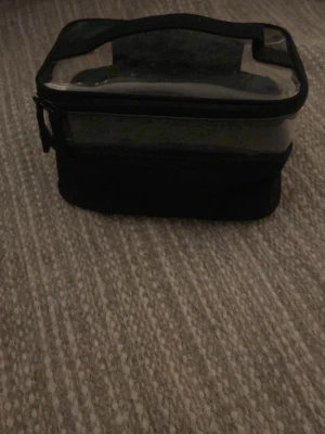 Transparent necessär från H&M Beauty - Snygg och praktisk necessär från H&M Beauty med transparent ovansida och svart botten. Perfekt för att organisera smink eller småprylar. Väskan har dragkedja och handtag upptill för enkel transport. Tillverkad i plast och textil.Är lite smutsig men såklart ska tvättas inna jag sickar 💕