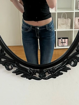 Mörkblå low waist jeans - Säljer ett par mörkblå low waist jeans med smal passform och vita kontrastsömmar. Klassisk femficksmodell och stretchigt denimtyg som sitter snyggt på kroppen. Perfekta till en avslappnad och trendig look.