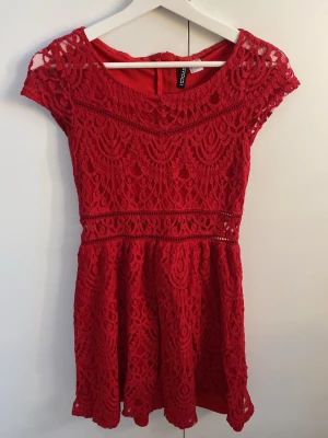 Röd spetsklänning från H&M - Kort röd klänning från H&M med vackert spetsmönster och rund halsringning. Klänningen har korta ärmar och markerad midja, samt dragkedja i ryggen. Perfekt för dig som vill ha en feminin och stilren look.