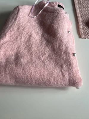Ljusrosa kofta med pärlknappar - Supersöt ljusrosa kofta från Gina Tricot med pärlknappar framtill. Koftan är stickad i ett mjukt material och har rund halsringning samt ribbade muddar. Perfekt för att addera en gullig touch till din outfit.aldrig använd🤍🎀