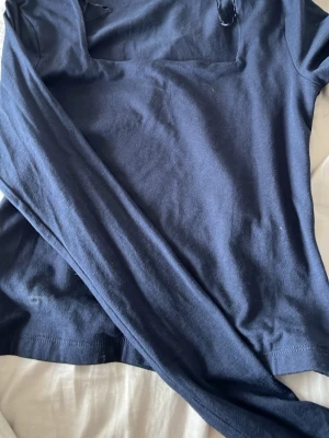 Mörkblå långärmad t-shirt - En enkel och stilren mörkblå långärmad t-shirt i mjukt bomullsmaterial. Perfekt för dig som gillar basic plagg med en clean look. Tröjan har rund hals och normal passform, vilket gör den lätt att matcha med jeans eller joggers.En fläck på men ska tvättas 
