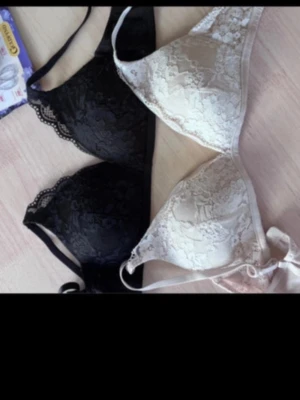 Två spetsbhar i svart och beige - Säljer två snygga bhar i spets, en i svart och en i beige/ljusrosa. Båda har tunna axelband och dekorativa spetsdetaljer över hela kupan. Perfekta för dig som gillar en feminin och stilren look. Materialet är mjuk spets och de har ingen synlig bygel.