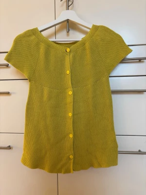 Gul stickad kortärmad kofta från Noa Noa storlek 152 XXS - Säljer en stickad gul kofta med korta ärmar och rund hals. Koftan har knappar framtill i samma färg och är tillverkad i bomull. Från Noa Noa storlek 152/ XXS