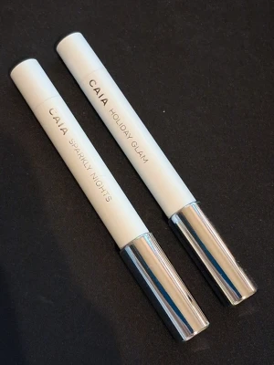CAIA ögonskuggspennor Holiday Glam - Två ögonskuggspennor från CAIA i nyanserna Holiday Glam och Sparkly Nights. Pennorna har vit kropp med silverfärgat lock och är enkla att applicera tack vare sin smidiga pennform. Perfekta för att skapa glittriga och festliga ögonmakeuper.