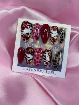 CherrySafari (M); Medium Almond - Snygga handgjorda press-on naglar i en medium mandelform. Mix av vinrött, vitt och svart med zebra-mönster, hjärtan och gulddetaljer. Perfekt för dig som vill sticka ut.M: 16 mm, 12 mm, 12,5 mm, 11,5 mm, 10 mm