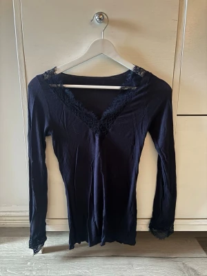 Svart långärmad topp med spets från Intimissimi  - Snygg svart långärmad topp med v-ringning och spetsdetaljer vid halsringning och ärmslut från Intimissimi. Tunn och mjuk i materialet, perfekt för lager på lager eller som den är. Enkel men ändå elegant design som passar till mycket. Den är använd fåtal gånger💕