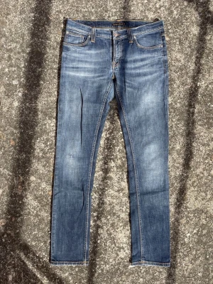 NUDIE JEANS MED SJUK WASH  - Snygga blå slim fit jeans från Nudie Jeans med klassisk femficksdesign och subtila slitningar. Jeansen har kontrastsömmar och läderpatch bak i midjan. Tillverkade i mjuk denim med stretch för extra komfort. Modell: Long John