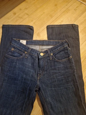 Mörkblå Lee bootcut jeans - Säljer ett par klassiska mörkblå jeans från  Lee med bootcut. Står ej någon storlek men måtten är:                               midjemått ca 30 cm             Innerbenslängd ca 74 cm